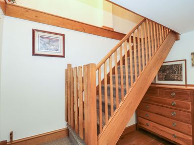 A wooden staircase with carpeted steps and a wooden chest of drawers beneath it at Oak Barn Kentisbeare