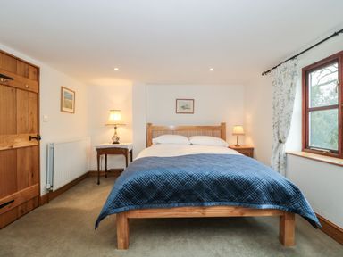 A bedroom with a wooden bed and blue quilt and two bedside tables with lamps at Oak Barn Kentisbeare