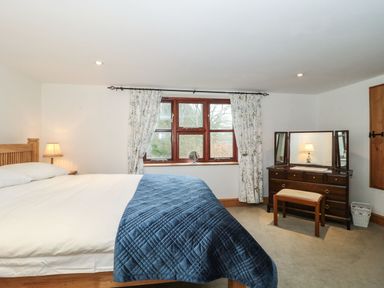A bedroom with a bed lamp window with curtains and a dressing table with stool at Oak Barn in Kentisbeare