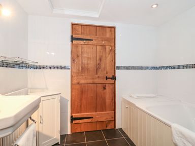 A bathroom with a wooden door a sink a white cabinet and a bathtub at Oak Barn in Kentisbeare