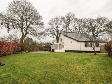 A backyard with green grass trees and a house with a white exterior at Oak Barn in Kentisbeare