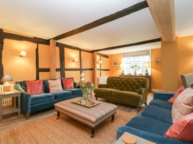 A living room with blue and green sofas a striped ottoman and flowers on a table at Byways in Madresfield near Malvern
