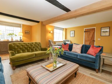 A living room with green and blue sofas a striped ottoman a wooden door and windows at Byways Madresfield near Malvern