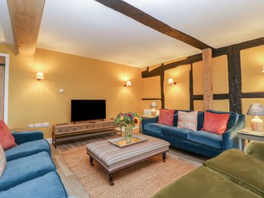 A living room with sofas a striped ottoman and a television at Byways Madresfield near Malvern