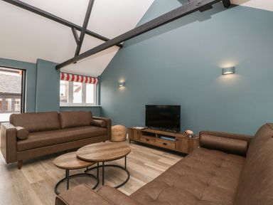 A living room with two brown sofas a wooden coffee table a wooden TV stand with a television and teal walls at Byways in Madresfield near Malvern
