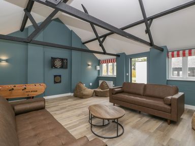 A game room with two brown sofas a round wooden coffee table bean bags dartboards foosball table and exposed beams at Byways Madresfield near Malvern