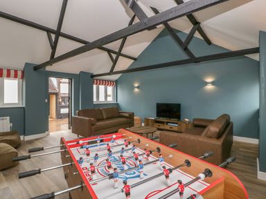 A game room with a foosball table two brown sofas a television and exposed ceiling beams at Byways Madresfield near Malvern