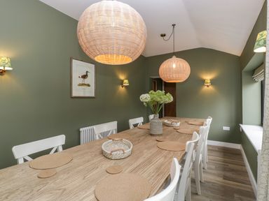 A dining room with a wooden table and white chairs with green walls and pendant lights at Byways in Madresfield near Malvern
