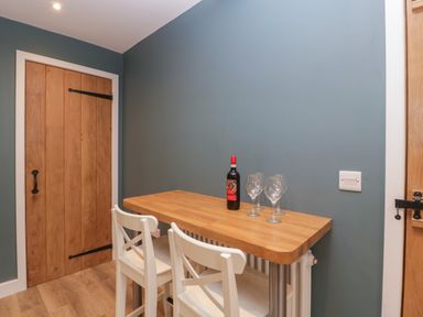 A small wooden table with a bottle of wine and three wine glasses with two white chairs next to wooden doors at Byways in Madresfield near Malvern