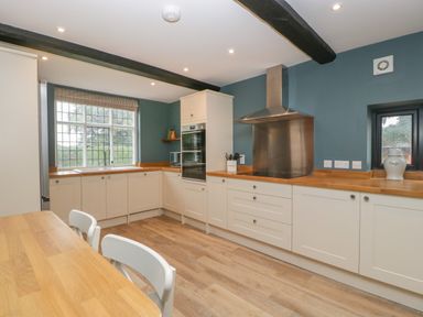 A kitchen with wooden countertops white cabinets a large window and a dining table with chairs at Byways in Madresfield near Malvern