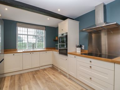 A kitchen with white cabinets wooden countertops a large window and stainless steel appliances at Byways in Madresfield near Malvern
