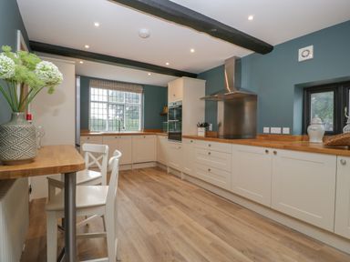 A kitchen with white cabinets wooden countertops wooden floor a window and two white chairs at Byways Madresfield near Malvern