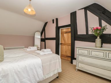 A bedroom with a bed with white bedding a dresser with a vase of flowers and a wooden door at Byways in Madresfield near Malvern