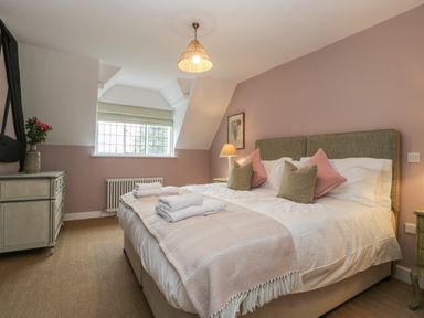 A bedroom with a bed with pillows and folded towels a bedside table with a lamp a chest of drawers with a vase of flowers and a window at Byways in Madresfield near Malvern