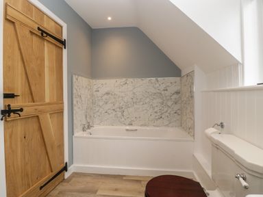 A bathroom with a wooden door a bathtub with marble surround and a toilet with a wooden seat at Byways in Madresfield near Malvern