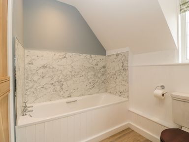 A bathroom with a bathtub marble wall panels a toilet with a dark seat and a window at Byways in Madresfield near Malvern