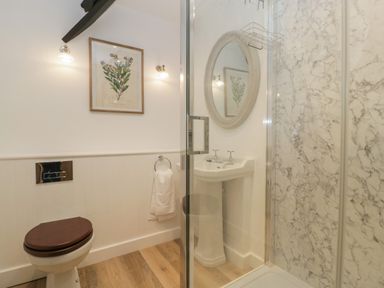 A bathroom with a toilet with wooden seat sink with oval mirror and a shower with marble walls at Byways in Madresfield near Malvern