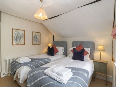 A bedroom with two single beds each with pillows and folded towels bedside tables with lamps and framed leaf prints on the wall at Byways Madresfield near Malvern