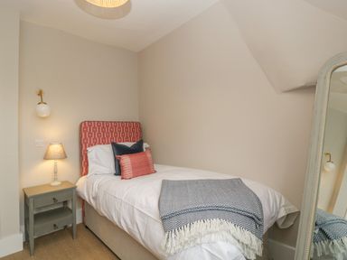 A bedroom with a bed with red headboard and pillows a bedside table with a lamp and a floor mirror at Byways in Madresfield near Malvern
