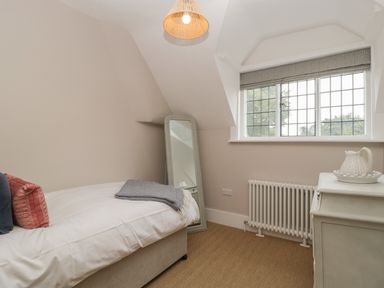 A small bedroom with a single bed pillows and blanket a standing mirror a radiator and a window with blinds at Byways Madresfield near Malvern