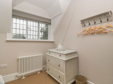 A small room with a window radiator chest of drawers a ceramic pitcher a hanging rack with wooden hangers and a wicker basket at Byways Madresfield near Malvern