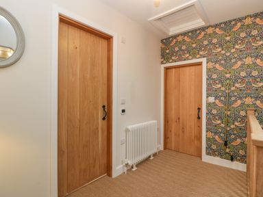 A hallway with two wooden doors a white radiator patterned wallpaper on one wall and a staircase railing at Byways Madresfield near Malvern