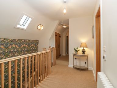 A hallway with wooden railing wallpaper on one wall and a small table with a lamp and flowers at Byways Madresfield near Malvern