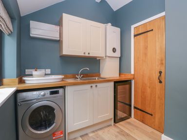 A utility room with a washing machine sink wooden counter cabinets and a wooden door at Byways Madresfield near Malvern