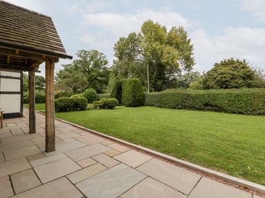A garden with trimmed hedges trees and grass next to a stone patio at Byways in Madresfield near Malvern