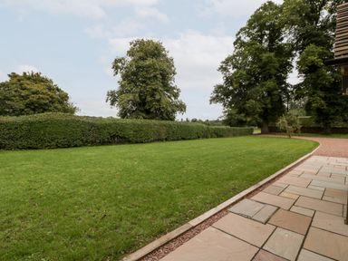 A grass lawn with hedges and trees beside a stone patio at Byways in Madresfield near Malvern