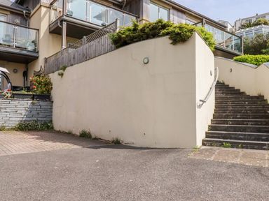 An outdoor stairway with handrail next to a courtyard and residential balconies at Pebbles in Downderry
