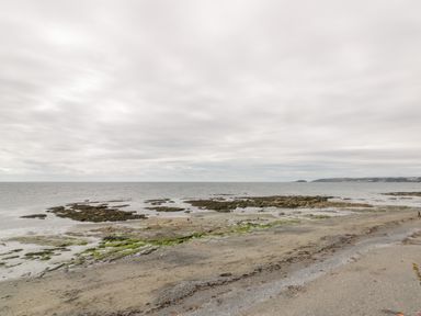 A rocky shoreline with sandy beach under a cloudy sky at Pebbles in Downderry