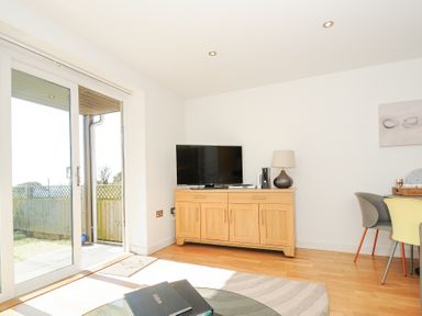A living room with wooden cabinet and TV near glass sliding door at Pebbles in Downderry