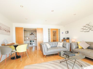 A living room with gray sofas a glass coffee table and dining table with chairs at Pebbles in Downderry