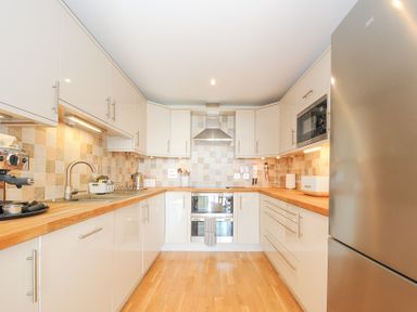 A kitchen with white cabinets wooden countertops stainless steel appliances and a tiled backsplash at Pebbles in Downderry