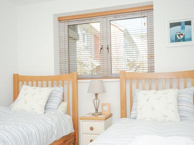 A bedroom with two single beds with striped bedding and a nightstand with a lamp and clock between the beds at Pebbles in Downderry