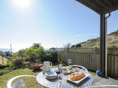 A garden with a table set with wine and food overlooking the sea at Pebbles in Downderry