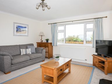 A living room with a grey sofa wooden coffee table wooden cabinet and television at 7 Maes Awel in Abersoch