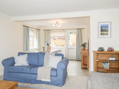 A living room with a blue sofa and dining table next to a window and door at 7 Maes Awel in Abersoch