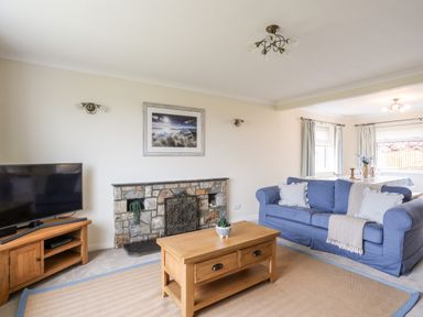 A living room with a blue sofa a wooden coffee table a stone fireplace and a TV at 7 Maes Awel in Abersoch