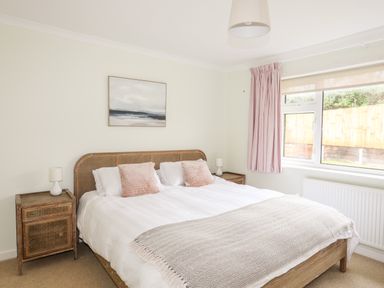 A bedroom with a double bed pillows bedside tables lamps and a window with curtains at 7 Maes Awel in Abersoch