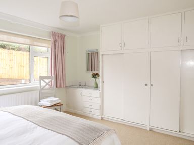 A bedroom with a bed a chair with towels a sink with a mirror and built in cupboards at 7 Maes Awel in Abersoch