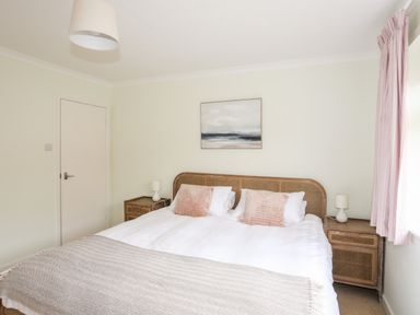 A bedroom with a bed with white linens and pink pillows and bedside tables with lamps at 7 Maes Awel in Abersoch