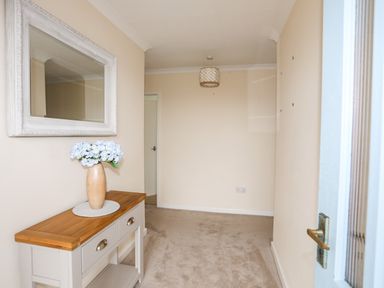 A hallway with a console table holding a vase of flowers and a mirror above at 7 Maes Awel in Abersoch