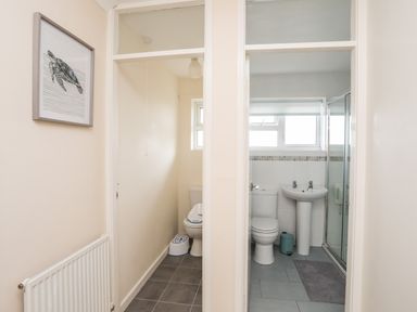 A hallway showing a toilet room on the left and a bathroom with a toilet sink and shower on the right at 7 Maes Awel in Abersoch