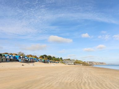 A sandy beach with colorful beach huts and buildings near the shoreline at 7 Maes Awel in Abersoch