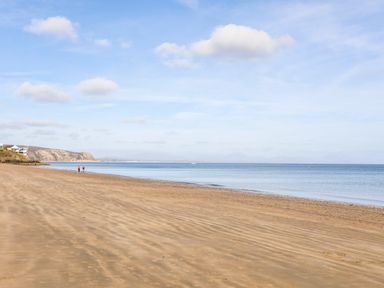 A sandy beach with two people walking near the shoreline and hills in the background at 7 Maes Awel in Abersoch