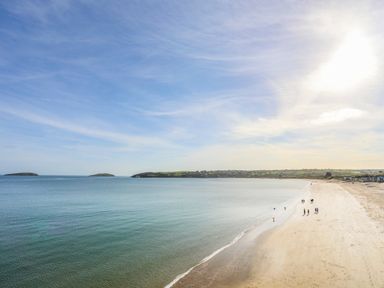 A beach with people walking near the water and small islands in the distance at 7 Maes Awel in Abersoch