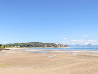 A sandy beach with small pools of water and hills in the background at 7 Maes Awel in Abersoch