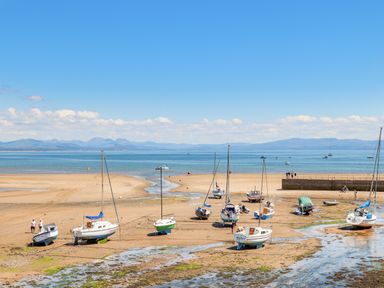 A sandy beach with several sailboats and boats resting on the shore near a concrete pier at 7 Maes Awel in Abersoch